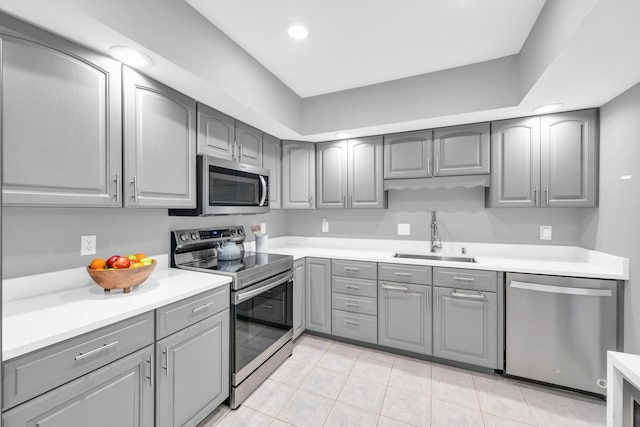 kitchen featuring gray cabinetry, stainless steel appliances, a sink, light tile patterned flooring, and light countertops