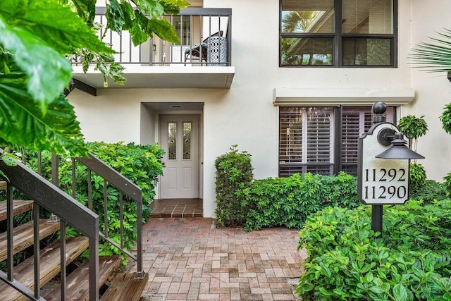 view of exterior entry with stucco siding and a balcony
