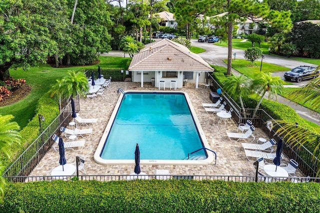 community pool with fence, a patio, view of wooded area, and an outbuilding