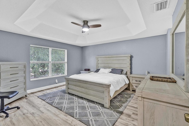 bedroom featuring a tray ceiling, light wood-style floors, baseboards, and a ceiling fan