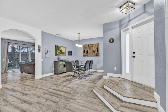 foyer featuring wood finished floors, arched walkways, and baseboards
