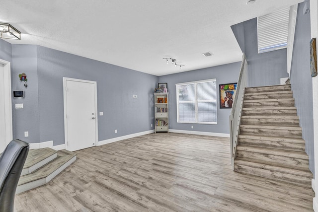 unfurnished living room featuring wood finished floors, stairway, and baseboards