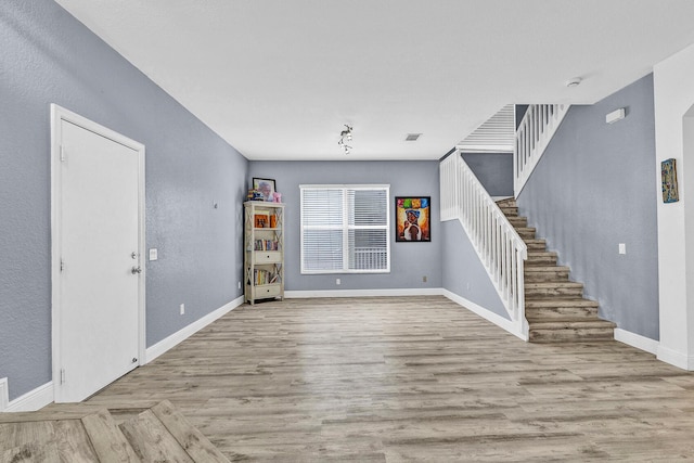 unfurnished living room featuring stairs, baseboards, wood finished floors, and a textured wall