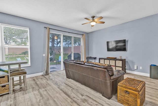 living area with a ceiling fan, light wood-type flooring, healthy amount of natural light, baseboards, and a textured ceiling