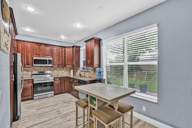 kitchen featuring appliances with stainless steel finishes, tasteful backsplash, light wood-style flooring, a sink, and a textured wall