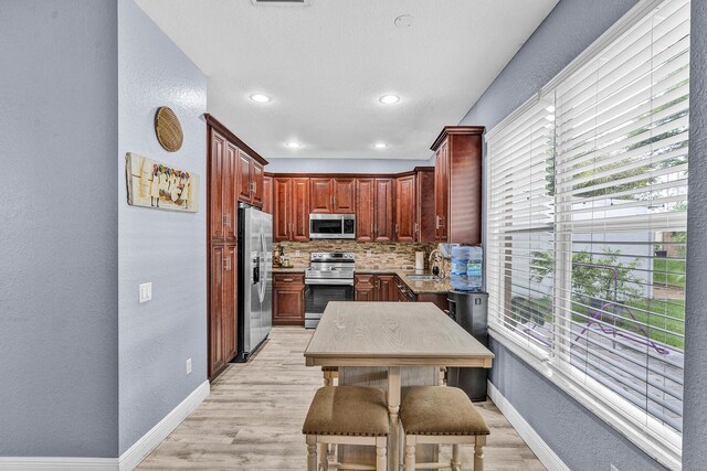kitchen featuring appliances with stainless steel finishes, a textured wall, baseboards, decorative backsplash, and light wood-style floors