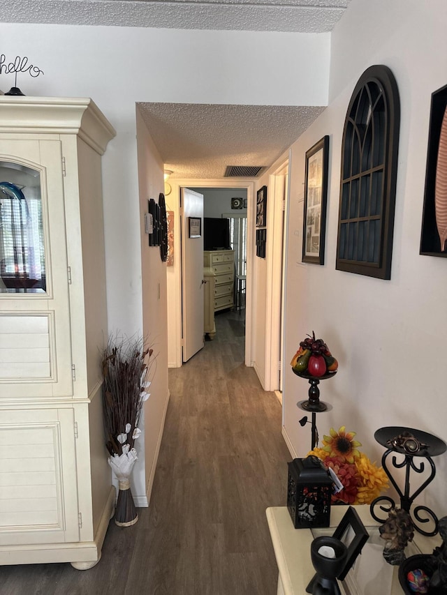 hallway with a textured ceiling, visible vents, wood finished floors, and baseboards