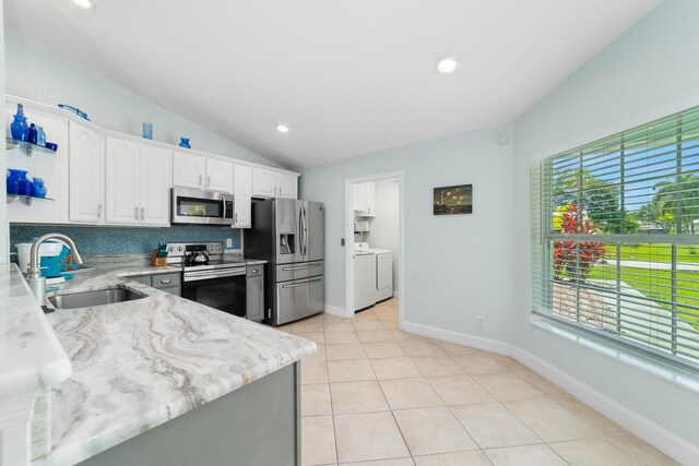 kitchen with stainless steel appliances, a sink, washing machine and dryer, vaulted ceiling, and decorative backsplash