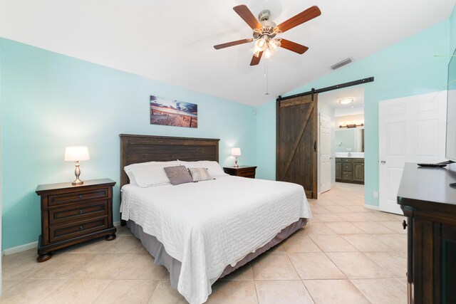 bedroom with a barn door, lofted ceiling, light tile patterned flooring, baseboards, and ensuite bathroom
