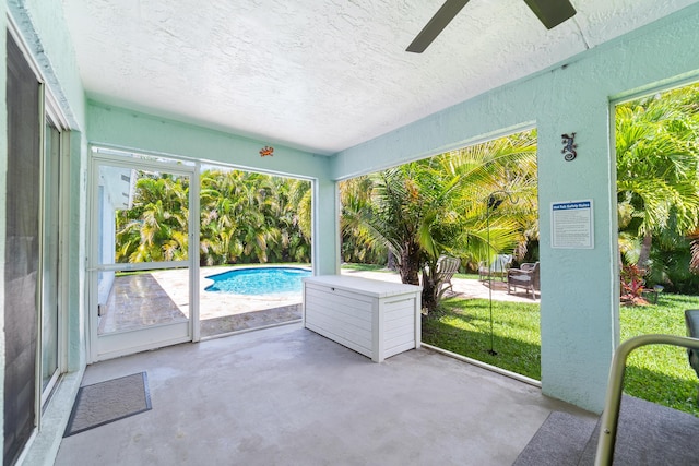 unfurnished sunroom featuring a ceiling fan, concrete floors, a textured ceiling, and a textured wall