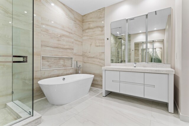 bathroom featuring a shower stall, marble tiled floors, vanity, a freestanding bath, and tile walls