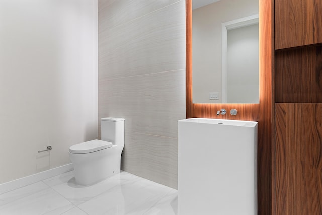 half bathroom with toilet, marble look tile flooring, and baseboards