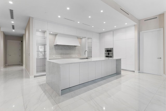 kitchen featuring modern cabinets, premium range hood, a sink, white cabinetry, and light countertops
