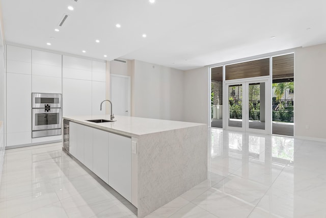 kitchen with modern cabinets, a sink, white cabinets, an island with sink, and light marble finish floors