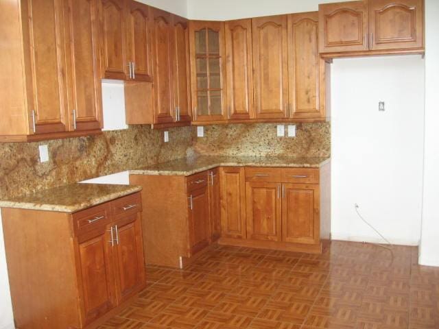 kitchen featuring brown cabinetry, light stone countertops, decorative backsplash, and glass insert cabinets