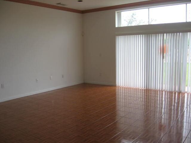 empty room with crown molding, visible vents, and baseboards