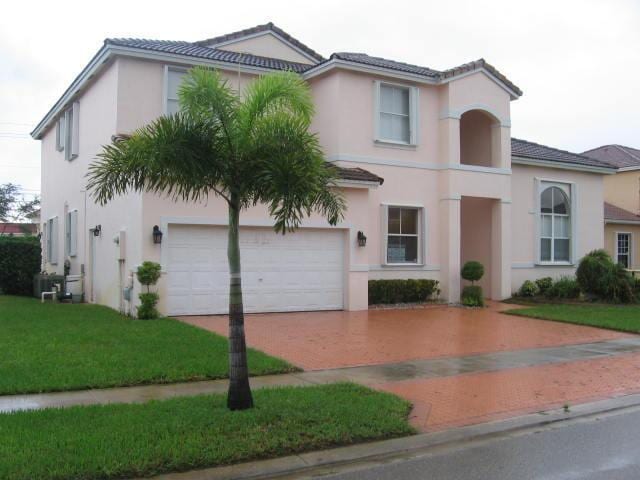 view of front of house with a tile roof, stucco siding, a front lawn, and decorative driveway