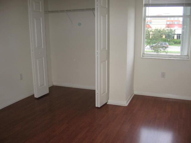unfurnished bedroom featuring baseboards, dark wood-style flooring, and a closet