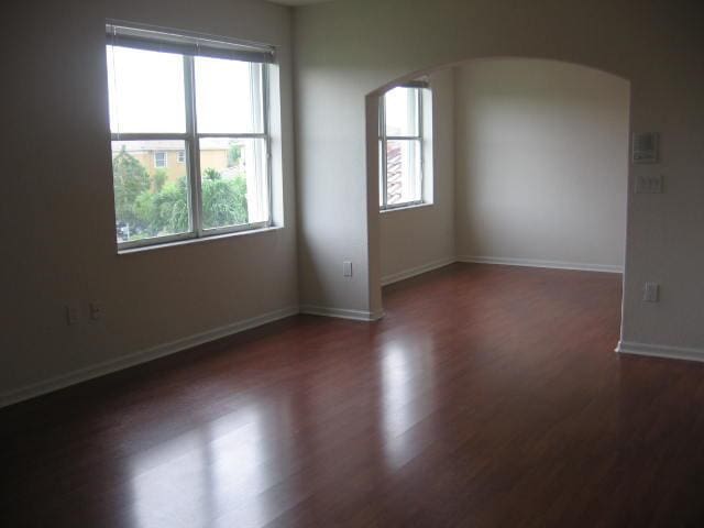 spare room with wood finished floors, baseboards, and arched walkways
