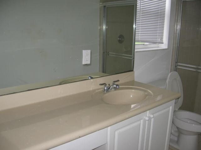 full bathroom with toilet, a shower with door, and vanity