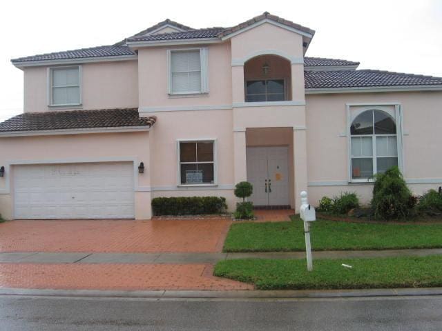 mediterranean / spanish home featuring stucco siding, an attached garage, a tiled roof, and decorative driveway