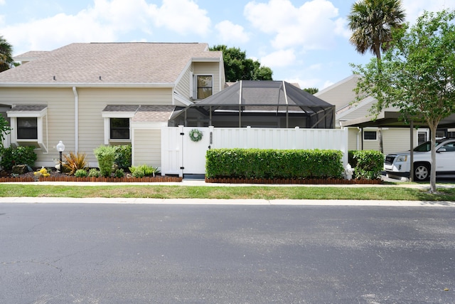 view of front of house featuring a shingled roof, fence, and a lanai