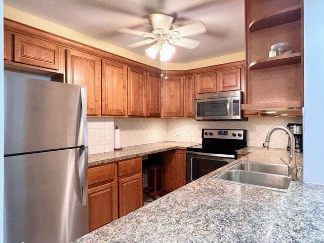 kitchen with a sink, stainless steel appliances, a ceiling fan, and brown cabinets