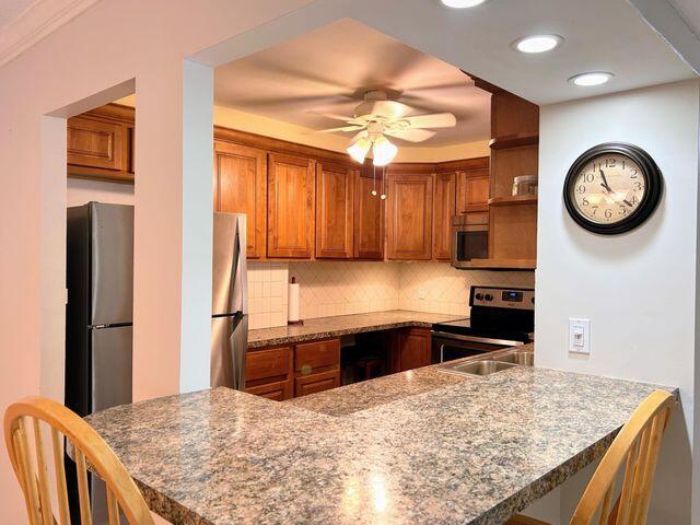 kitchen featuring a peninsula, brown cabinets, backsplash, and appliances with stainless steel finishes