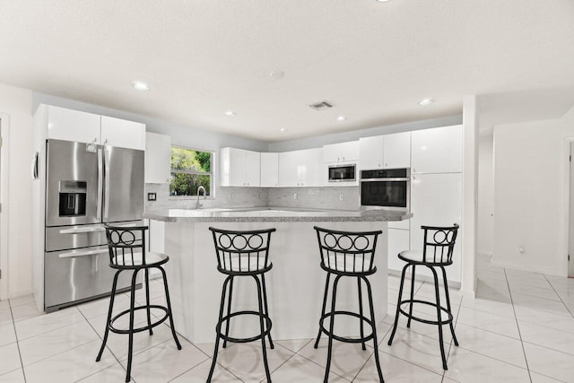 kitchen with appliances with stainless steel finishes, a kitchen bar, decorative backsplash, a kitchen island, and white cabinets