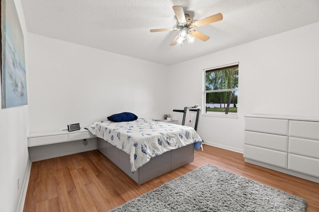 bedroom featuring light wood finished floors, baseboards, a ceiling fan, and a textured ceiling