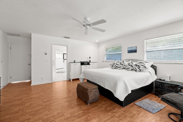 bedroom with light wood-type flooring, a textured ceiling, ceiling fan, and ensuite bathroom