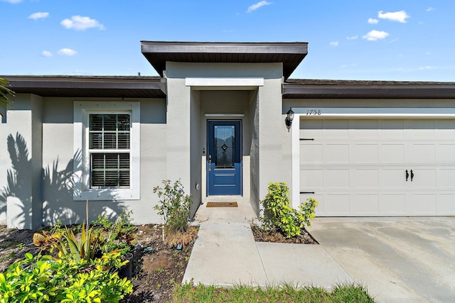 entrance to property featuring stucco siding, a garage, and concrete driveway
