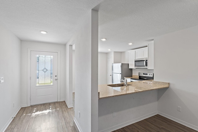 kitchen featuring appliances with stainless steel finishes, wood finished floors, light stone countertops, white cabinetry, and baseboards