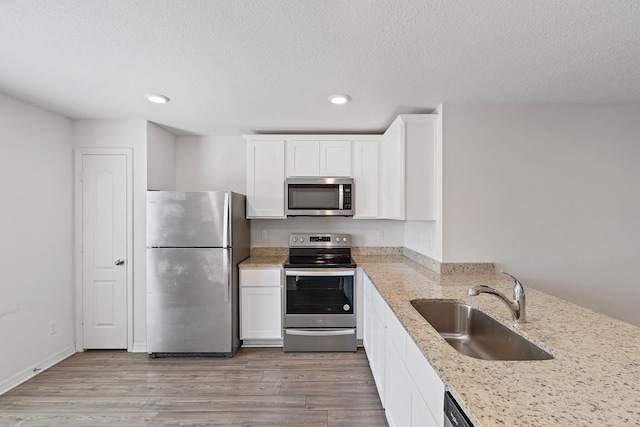 kitchen with stainless steel appliances, a sink, light stone countertops, recessed lighting, and white cabinetry
