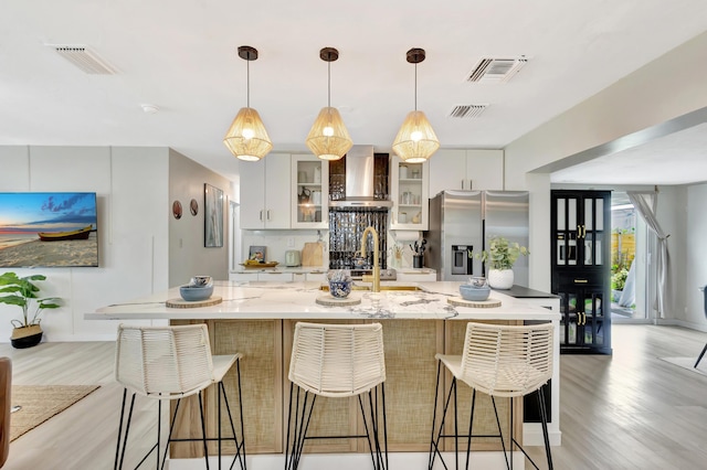 115 W 31st Ct, Riviera Beach, FL 33404 - kitchen with light wood finished floors, stainless steel refrigerator with ice dispenser, visible vents, and wall chimney exhaust hood