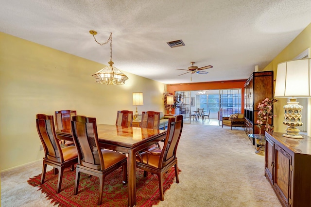 dining space with light colored carpet, a chandelier, a textured ceiling, and a ceiling fan