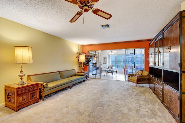 living area with ceiling fan, light colored carpet, and a textured ceiling