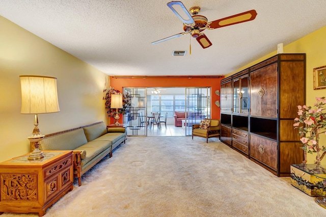 living room featuring a ceiling fan, light colored carpet, and a textured ceiling