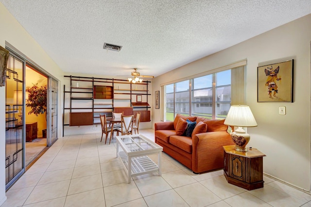 living room with ceiling fan, a textured ceiling, and light tile patterned flooring