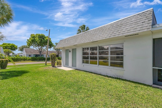 back of property featuring roof with shingles, stucco siding, a lawn, and mansard roof
