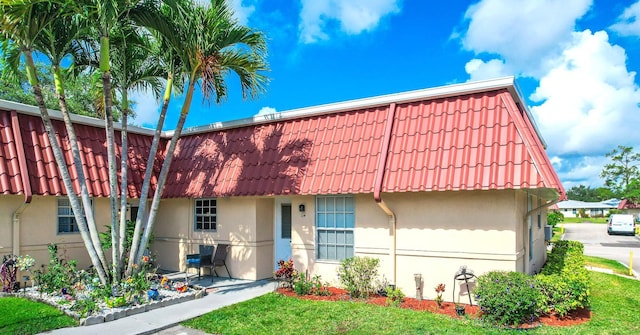 view of property with mansard roof, a front yard, stucco siding, and a tiled roof