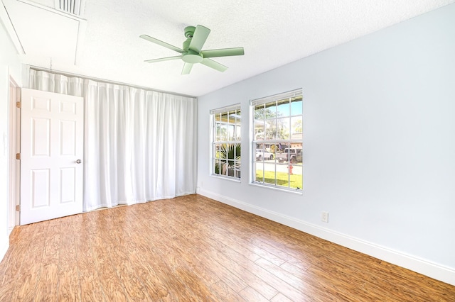 interior space with wood finished floors, a ceiling fan, attic access, a textured ceiling, and baseboards