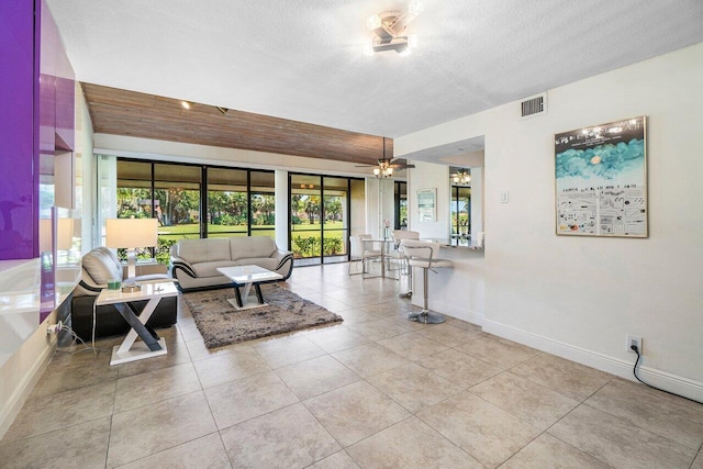 living area featuring baseboards, a textured ceiling, tile patterned flooring, and ceiling fan