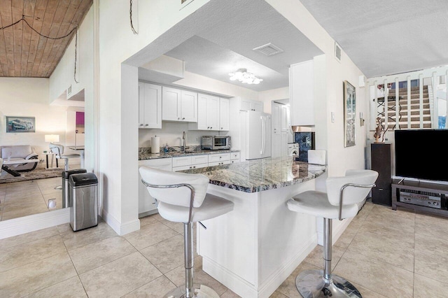 kitchen featuring freestanding refrigerator, a breakfast bar area, white cabinets, a sink, and a peninsula