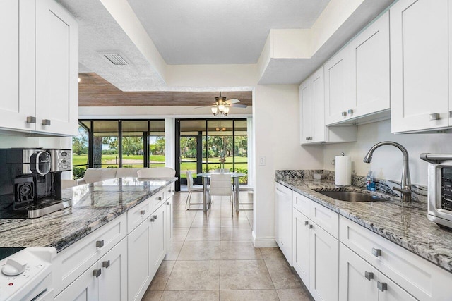 kitchen featuring a sink, plenty of natural light, white cabinetry, and a wood stove