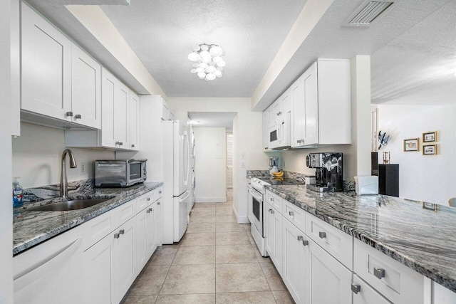 kitchen with white appliances, a sink, a textured ceiling, white cabinets, and dark stone counters