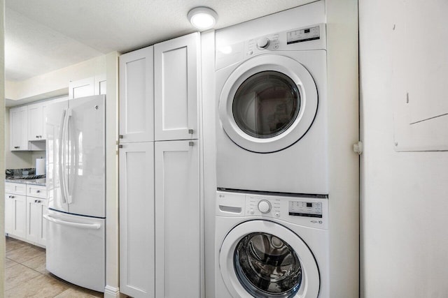 laundry room featuring stacked washing machine and dryer, cabinet space, a textured ceiling, and light tile patterned floors