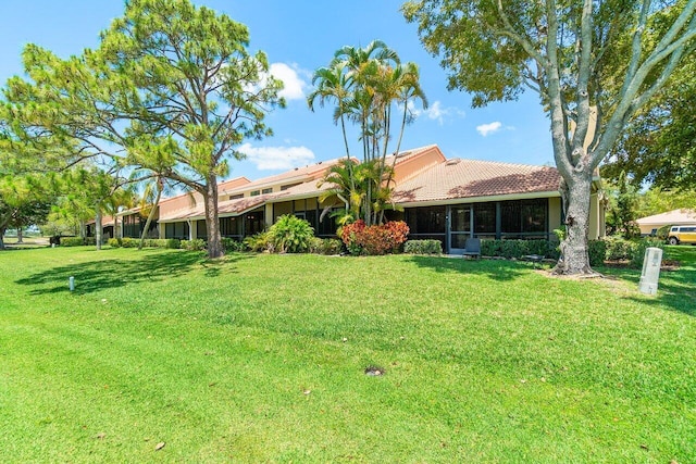 rear view of house with a yard, a tiled roof, and a sunroom