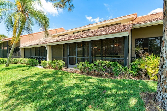 rear view of house featuring a tiled roof, a lawn, a sunroom, and stucco siding
