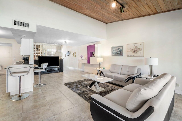 living room featuring wood ceiling, light tile patterned flooring, baseboards, and a high ceiling